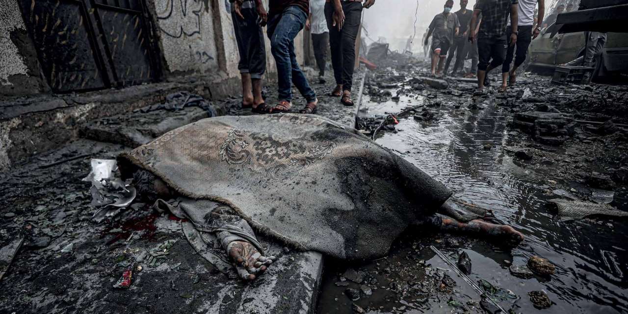 A Palestinian youth, killed in the Israeli army’s air strikes on the Ridwan neighborhood of Gaza, lies on the ground, covered by the survivors.